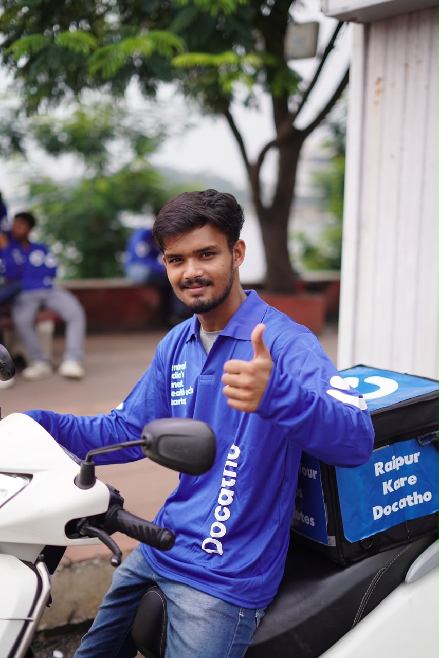 A Docatho rider on a scooter with a Raipur Kare Docatho delivery box, thumbs up