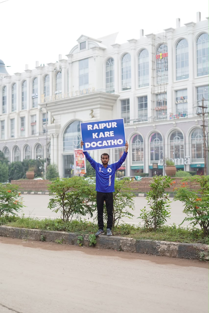 A Docatho rider holding a Raipur Kare Docatho board outside Currency Tower